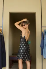 Vestido corto negro de cuero genuino, con diseño de autor inspirado en Paco Rabanne. La prenda está confeccionada manualmente uniendo piezas de cuero en forma de rombos, sujetas con argollas metálicas, creando un efecto de cota de malla con caída asimétrica en el ruedo. Posee tirantes finos.