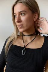 Collar con doble tira de tiento negro, una ajustada al cuello como choker y otra más larga con un dije ovalado de piedra natural blanca y un pequeño detalle dorado.