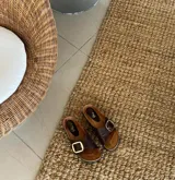 Sandalias de cuero color chocolate con hebilla dorada ajustable.