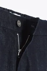 Pantalón bombacho de denim azul oscuro, tiro medio, con bolsillos laterales ocultos y de parche en la espalda. Presenta pinzas en la parte delantera y bajo abullonado con elástico.
