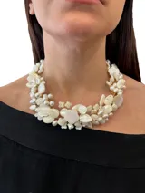Collar corto hecho a mano con piezas de nácar blanco en forma de pétalos y perlas, engarzadas con hilo dorado. Cierre de mosquetón con cadena regulable.