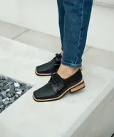 Zapato acordonado de cuero vacuno color marrón oscuro, con suela de goma, horma cuadrada y tacón bajo.