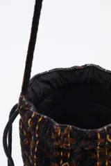 Bolso tipo saco o 'bucket bag' de terciopelo con estampado animal print en tonos marrón oscuro y negro. Presenta costuras verticales en hilo dorado y cordones ajustables negros con borlas y cuentas doradas en los extremos.