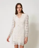 Vestido corto color blanco de encaje macramé con diseño geométrico, escote de pico, mangas largas abullonadas tipo guante con cremallera invisible en el bajo, cierre de cremallera en el lateral, bajo festoneado, forro de muselina de algodón y cinturón extraíble a juego con elástico y hebilla con el logotipo Oval T dorado, de corte recto.