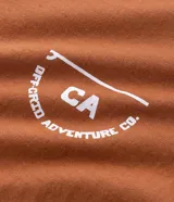 Remera masculina color marrón, de corte comfort, con cuello redondo y mangas cortas. Presenta un estampado de letras "Travelers" en el pecho y la espalda.