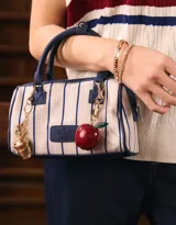 Cartera bowling con estampado de rayas verticales color beige y azul marino. Tiene doble asa corta de mano y correa regulable y desmontable. Incluye cierre superior y tag frontal de cuerina con el logo 'The Brunch Club'.