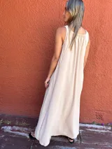 Vestido midi de seda opaca color camel, con silueta en A, cuello redondo y sin mangas. Presenta bolsillos laterales, cortes laterales y un detalle de diseño en la espalda.