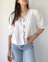 Camisa blanca de mangas 3/4 con detalle de volados en los puños y botones de madera.