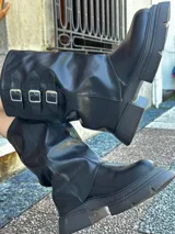 Botas de caña media de cuero sintético negro con suela track y tres hebillas decorativas.