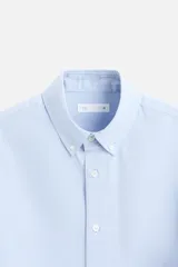 Camisa celeste de algodón, corte relaxed fit, cuello abotonado, manga larga con puños abotonados y cierre frontal con botones.