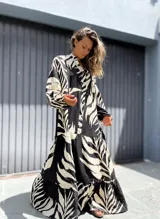Vestido largo de manga larga, con cuello camisero y estampado de hojas tropicales en blanco y negro. El diseño presenta un corte amplio con volados en la falda.