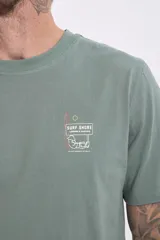 Remera de algodón color verde salvia, con cuello redondo y manga corta. Presenta un pequeño parche estampado en el pecho con un diseño gráfico.