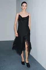 Vestido lencero de satén negro, corte midi asimétrico, con escote fluido y tirantes finos. Presenta drapeado lateral y aplicación de encaje a tono en el bajo.