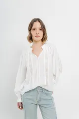 Blusa blanca de gasa liviana con detalles de encaje calado en el frente y mangas largas con puño elástico.