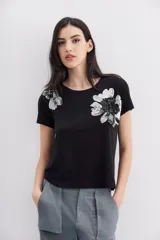 Remera negra de algodón con calce relajado, cuello redondo y mangas cortas. Presenta bordados florales con lentejuelas en el frente.