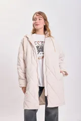 Campera larga color crudo con capucha y cierre frontal, diseño acolchado con patrón de rombos.