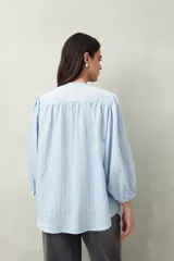 Camisa celeste a rayas verticales, de corte amplio y mangas 3/4. Presenta cuello mao, cierre frontal con botones irregulares y detalle de pespuntes y pinzas en el canesú.