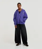 Canguro de algodón con felpa en color lila, con capucha ajustable, cierre frontal de cremallera y bolsillos delanteros. Presenta estampados de lettering en la espalda con diseños de estilo urbano.