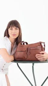 Bandolera color beige con correa ajustable, dos bolsillos frontales (uno con botón y otro con cierre) y un bolsillo trasero con cierre.