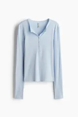 Remera ajustada de punto acanalado suave, color celeste, con manga larga, cuello redondo ribeteado en picot y tapeta de botones.