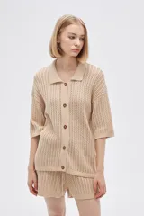 Remera de punto calado color beige, con cuello polo, mangas cortas y cierre frontal con botones.