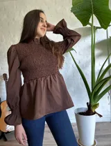 Blusa marrón con cuello alto fruncido, mangas largas abullonadas con puños elásticos y cuerpo con textura fruncida.