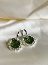 Aros colgantes con dije circular de resina verde con glitter, bordeado con strass plateado y arito de acero quirúrgico.