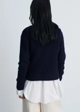 Chaqueta azul marino de punto medio con cuello de pico con solapa, cierre cruzado de doble botonadura con botones dorados efecto joya, diseño recto, solapas con muesca y dos bolsillos de parche frontales.