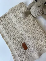Manta tejida de hilo de algodón color beige, con diseño calado y etiqueta de cuero con logo.