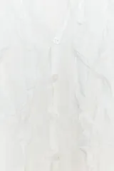 Top blanco semitransparente con escote en pico, sin mangas, tejido arrugado y volantes delanteros. Cierre frontal con botones.