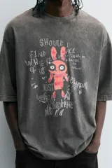 Camiseta gris con efecto lavado, cuello redondo y manga corta. Estampado frontal con conejo, texto y efecto de pintura.