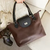 Cartera tote de cuero vacuno color marrón con solapa negra y cierre metálico.