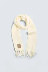 Bufanda color crema confeccionada en tejido con lana y acabado cepillado. Tiene flecos en los extremos.