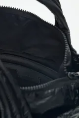 Cartera tote azul de nylon matelassé con diseño de corazones. Tiene manijas cortas y dos correas desmontables, una de cuero sintético y otra de tela trenzada multicolor. Cuenta con cierre superior y dos bolsillos internos.