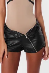 Short negro de cuerina con cierre diagonal desmontable, tiro medio y broches snap en el delantero.