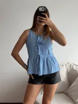 Blusa sin mangas con estampado a rayas verticales celestes y blancas, con escote en V y lazos decorativos. Corte peplum con frunce en la cintura.