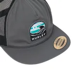 Gorro estilo trucker de color gris oscuro, con paneles traseros de malla negra. Presenta un parche frontal rectangular con un diseño de olas en tonos turquesa, blanco y gris, y el logo "HURLEY" en la parte inferior. Tiene visera plana y cordón decorativo en la unión de la visera y el cuerpo.