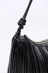 Cartera de hombro negra con diseño plisado vertical, asas largas con nudos decorativos y cierre de cremallera.