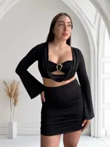 Vestido negro de tres piezas, compuesto por un top tipo corpiño con aro dorado, una falda mini fruncida y un cardigan de mangas largas.