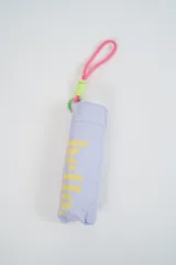 Paraguas plegable de color beige claro con la palabra "hello." estampada en azul. Incluye un asa de mano tipo correa en tonos amarillo y rosado.