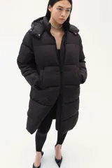 Campera puffer larga negra con capucha, cierre frontal y bolsillos insertados.