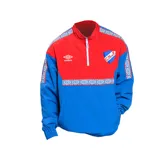 Buzo deportivo Umbro del Club Nacional de Football, con medio cierre frontal, diseño color rojo en la parte superior y azul en la inferior, con detalles de logos y patrones geométricos en cuello, hombros y mangas.