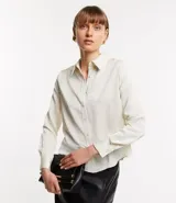 Camisa color crema en crepé con cuello solapa, abotonado frontal, mangas largas y textura de flores tramadas en el tejido.