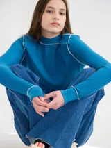 Polera negra de tela rib con cuello alto y mangas largas. Presenta pespuntes rojos en cuello, hombros y puños.