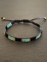 Pulsera tejida con cuentas Miyuki originales en tonos negro, turquesa y dorado. Ajustable con cordón negro.