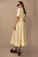 Vestido midi camisero color ladrillo, confeccionado en popelina de algodón. Presenta cuello solapa, manga corta con puños abotonados, bolsillos laterales ocultos y bolsillos de parche con solapa en el pecho. Incluye cinturón lazada en el mismo tejido y cierre frontal con botones ocultos.