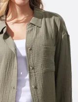 Camisa blanca de algodón con textura arrugada, cuello con solapa, abertura central con botones y bolsillo aplicado en el pecho. Mangas largas con largo regulable mediante presilla y botón.