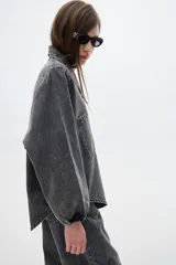 Camisa de jean oversized, color gris oscuro, con escote en V bajo, cuello camisero y mangas abullonadas. Tiene bolsillos delanteros y cierre con botones metálicos.