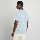 Remera tipo polo celeste de punto con cuello clásico y tres botones marrones.