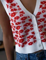 Chaleco tejido blanco con estampado floral rojo, escote en V y cierre frontal con botones.